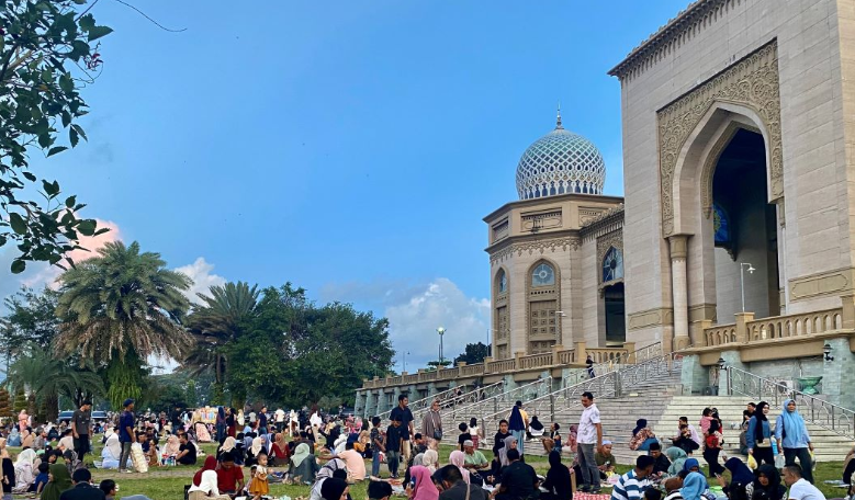 Sejumlah warga duduk lesehan di halaman Masjid Agung Islamic Center, Kota Lhokseumawe, sambil menikmati hidangan berbuka puasa di atas tikar pada Minggu, 16 Maret 2025. Di sekitarnya, terlihat pedagang keliling dan anak-anak yang berlarian, menciptakan suasana ramai dan hangat.
